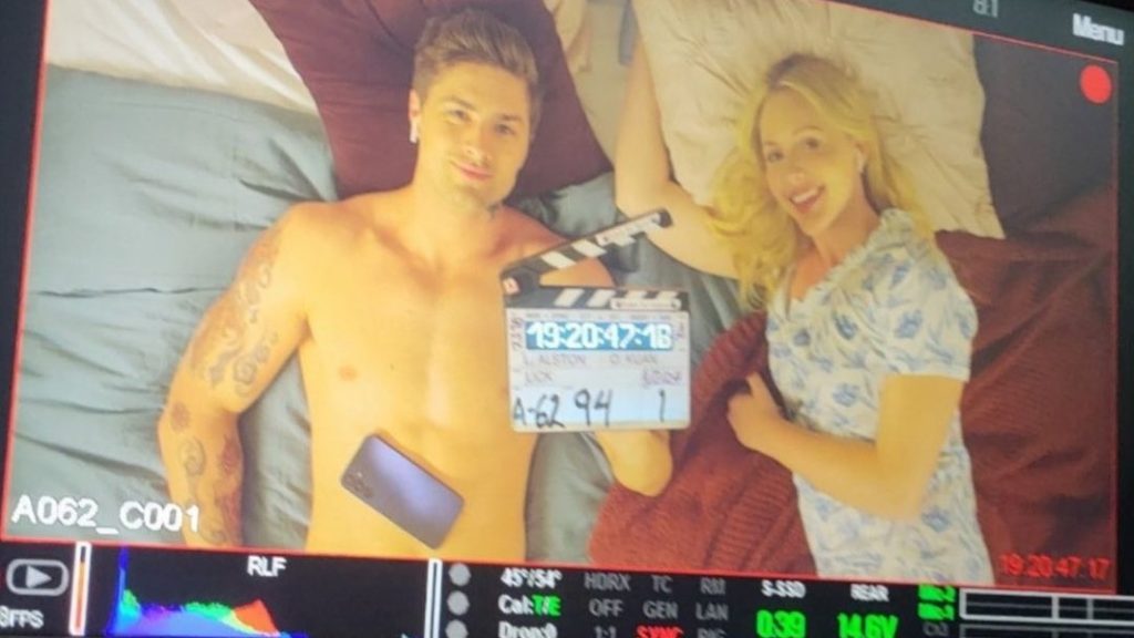 Brooke Lee and Travis Burns lie on a bed with the clapperboard for Lick.