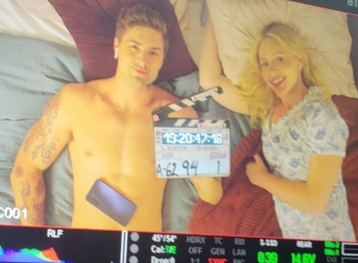 Brooke Lee and Travis Burns lie on a bed with the clapperboard for Lick.